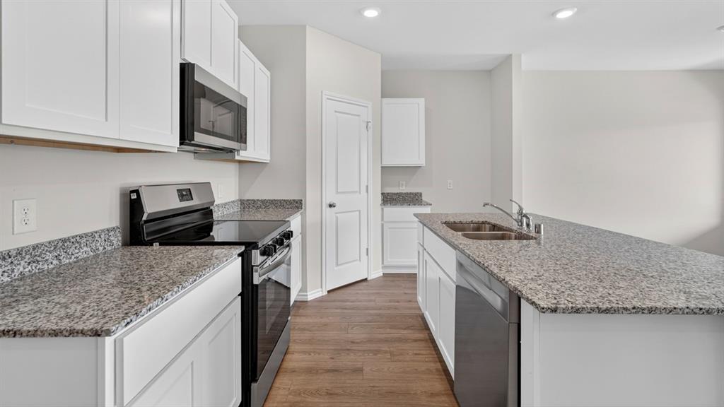 Modern kitchen featuring white shaker cabinetry, stainless steel appliances, speckled stone countertops, a double basin sink, and wood-finish flooring