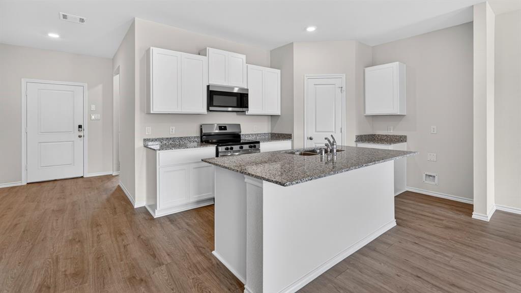 Kitchen featuring an island with a dual-basin sink, stainless steel appliances, granite countertops, white cabinetry, and wood-finish flooring