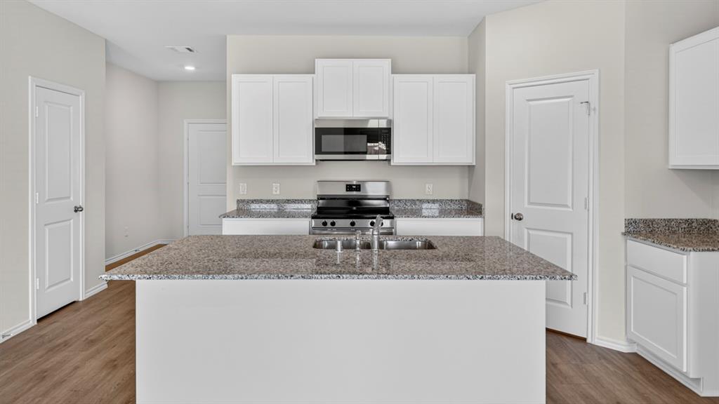Kitchen featuring a central island with an undermount sink, granite countertops, white cabinetry, stainless steel appliances, and wood-finish flooring