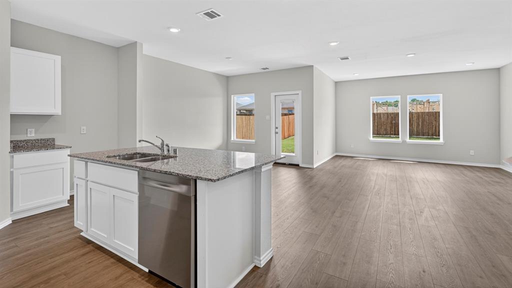 Open-concept kitchen and living area featuring wood-finish flooring, white cabinetry, granite countertops, and recessed lighting