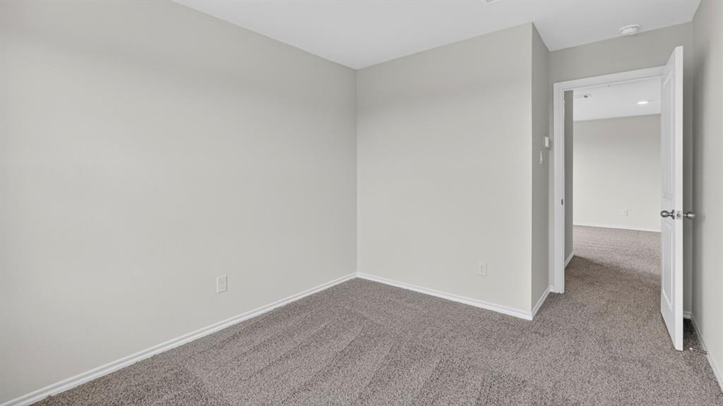 Room featuring light gray wall paint, gray carpeting, white baseboards, and a white interior door with a silver knob