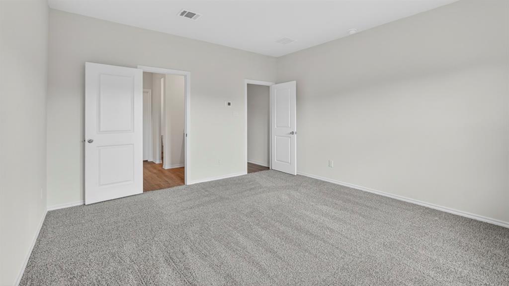 Spacious room featuring light gray walls, gray carpeting, white baseboards, and two-panel interior doors