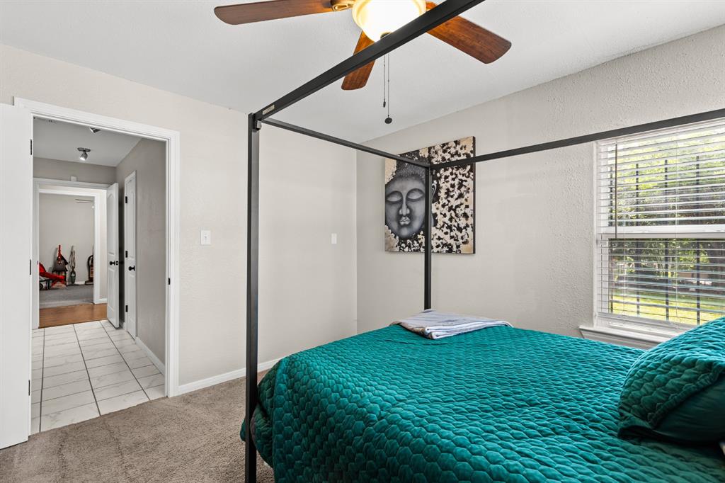 Carpeted bedroom featuring a ceiling fan with light fixture, window with blinds, and white painted walls