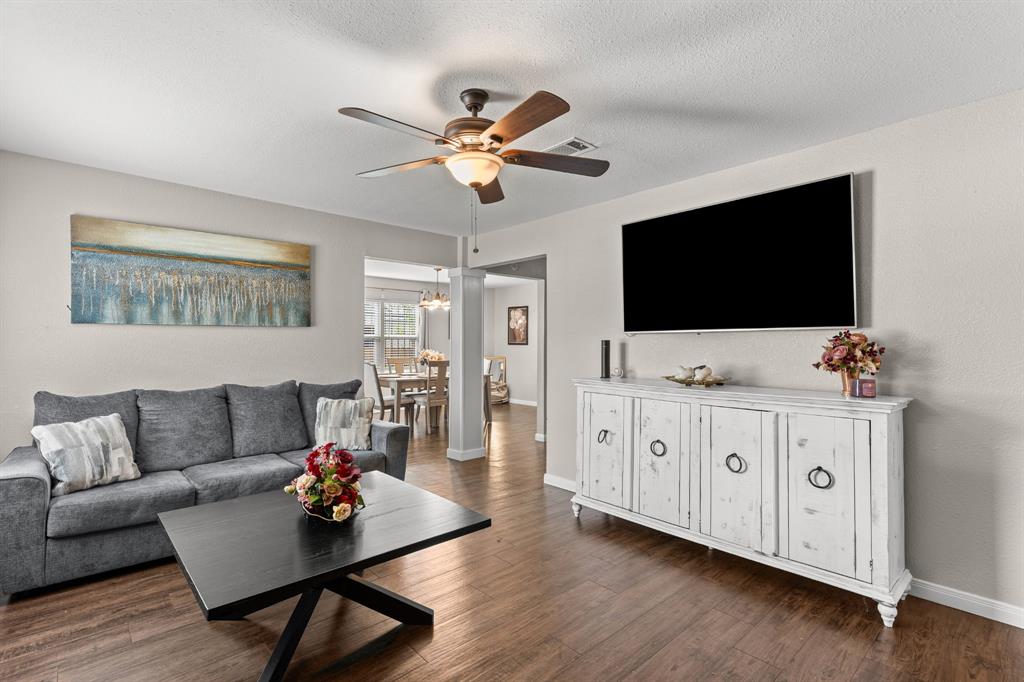 Open-concept living space featuring wood-finish flooring, a ceiling fan with integrated lighting, and neutral wall tones Open-concept living space featuring wood-finish flooring, a ceiling fan with integrated lighting, and neutral wall tones