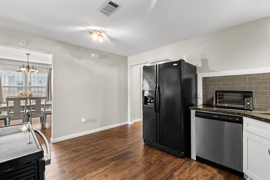 Kitchen featuring wood-finish flooring, white cabinetry, a dark subway tile backsplash, and a stainless-steel dishwasher Kitchen featuring wood-finish flooring, white cabinetry, a dark subway tile backsplash, and a stainless-steel dishwasher