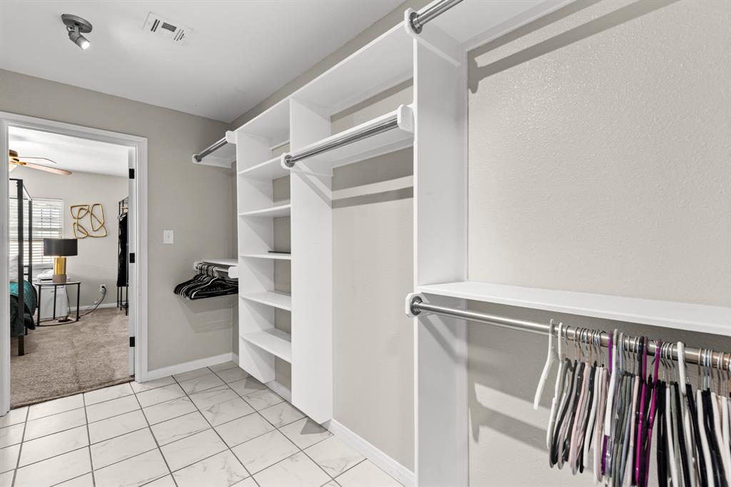 Walk-in closet featuring white built-in shelving, multiple hanging rods, and tile flooring