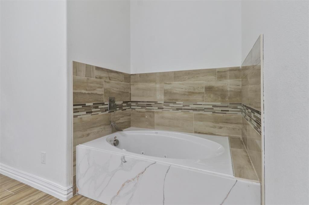 Spa-inspired primary bathroom featuring a freestanding soaking tub with integrated deck surround, horizontal wood-finish tile walls in warm neutral tones, and a coordinating tile accent stripe