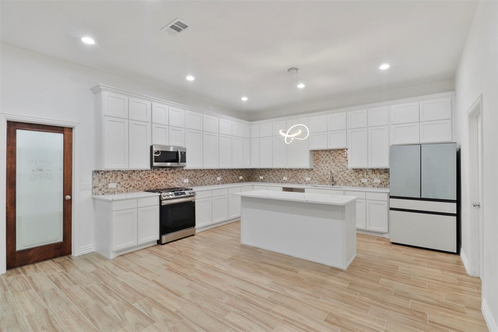 Modern kitchen featuring white cabinetry, stainless steel appliances, and a large center island with white countertop
