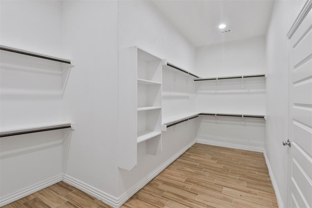 Spacious walk-in closet featuring wood-finish flooring, extensive built-in shelving, multiple hanging rods, recessed lighting, and a paneled interior door