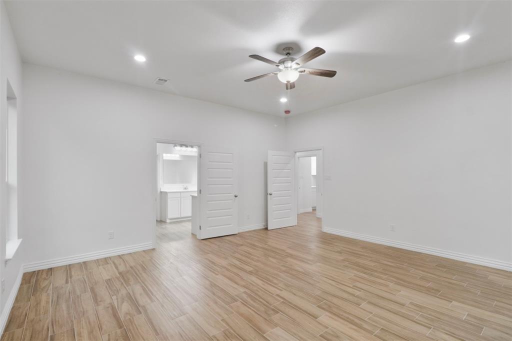 Spacious bedroom showcasing pristine white walls, wood-finish flooring throughout, and recessed ceiling lighting