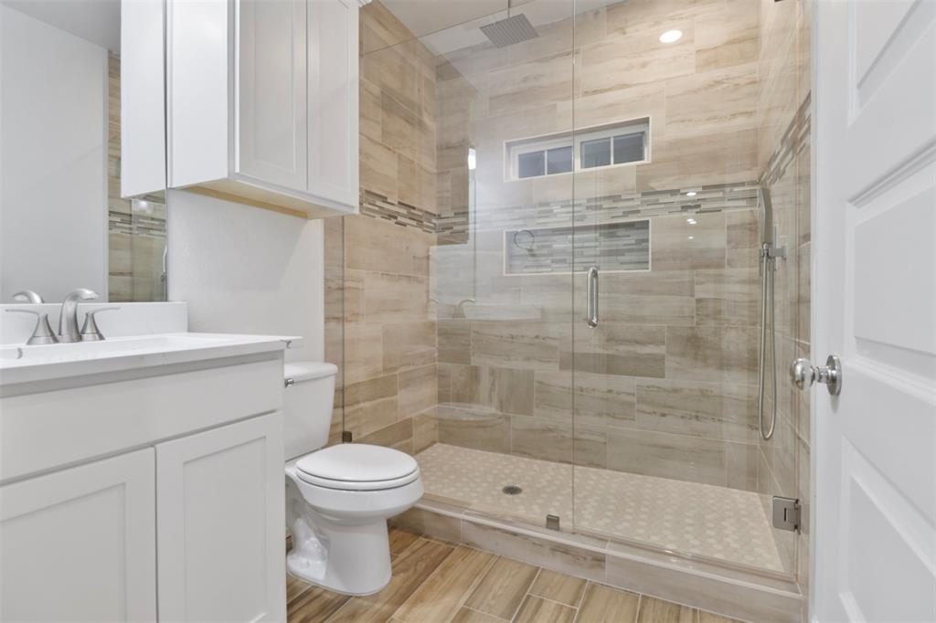 Spa-inspired primary bathroom featuring a frameless glass-enclosed shower with linear tile surround, dual showerheads, and a rainfall fixture