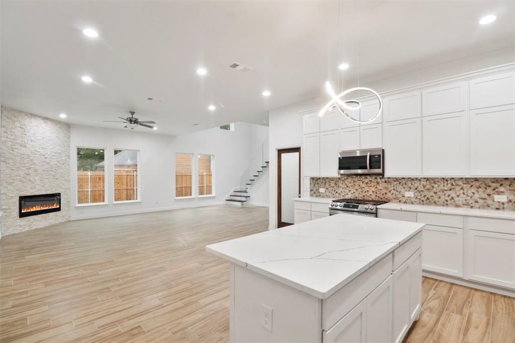 Open-concept living space featuring a chef's kitchen with white cabinetry, quartz waterfall island countertop, stainless steel appliances, and a tile backsplash