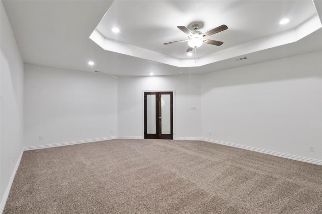 Spacious room featuring a tray ceiling with recessed lighting, a ceiling fan, plush carpet flooring, and dark wood-finish double doors with glass panels