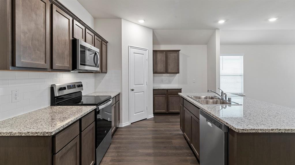Spacious kitchen featuring dark wood-finish cabinetry, light speckled countertops, stainless steel appliances, a subway tile backsplash, and wood-finish flooring