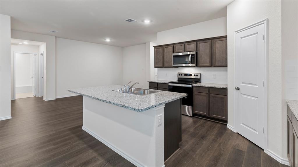 Kitchen featuring a central island with a double basin sink, granite-style countertop, and pendant lighting