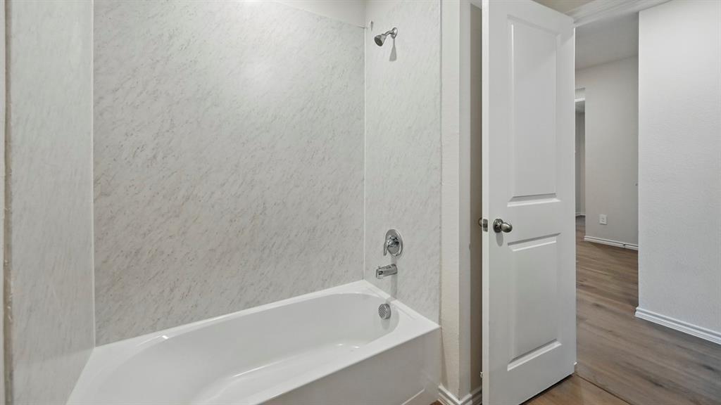 Bathroom featuring a white bathtub with a chrome faucet and shower head, surrounded by textured white wall panels Bathroom featuring a white bathtub with a chrome faucet and shower head, surrounded by textured white wall panels