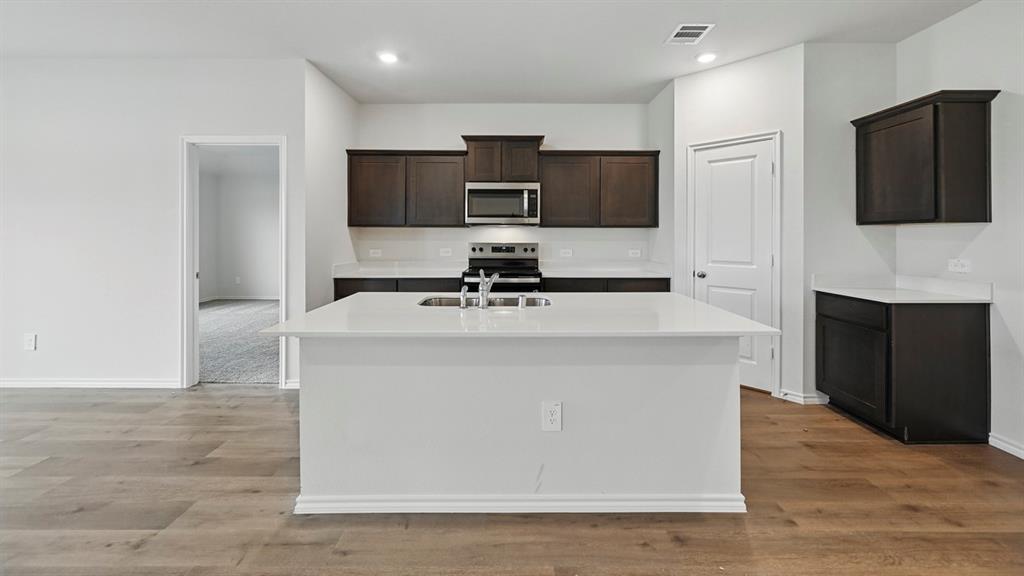 Kitchen featuring a central island with an undermount sink, dark wood cabinetry, stainless steel appliances, and wood-finish flooring