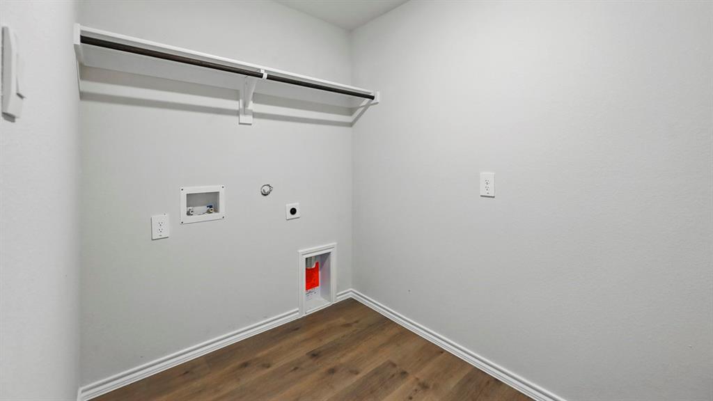 Dedicated laundry area featuring a white wire shelf, hanging rod, wood-finish flooring, and white baseboards