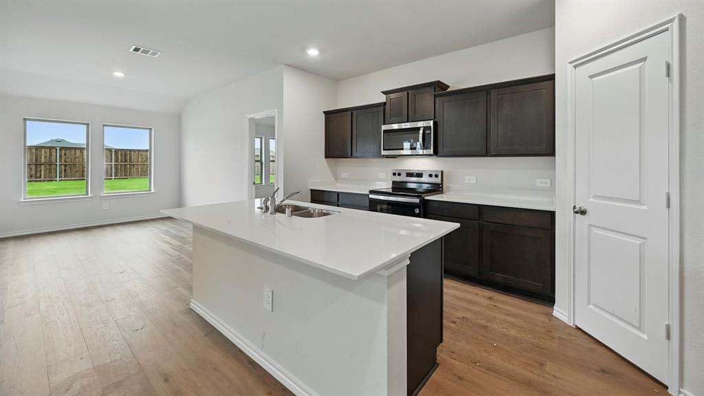 Kitchen featuring an island with an undermount sink, dark wood-finish cabinetry, stainless steel appliances, and light countertops