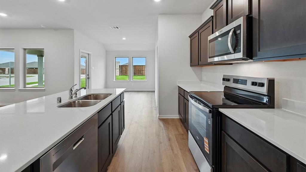 Modern kitchen featuring dark wood-finish cabinetry, stainless steel appliances, solid surface countertops, a double basin sink, and wood-finish flooring
