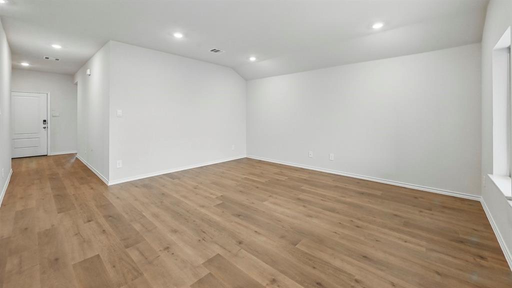 Spacious room featuring wood-finish flooring, recessed lighting, white baseboards, and a white interior door