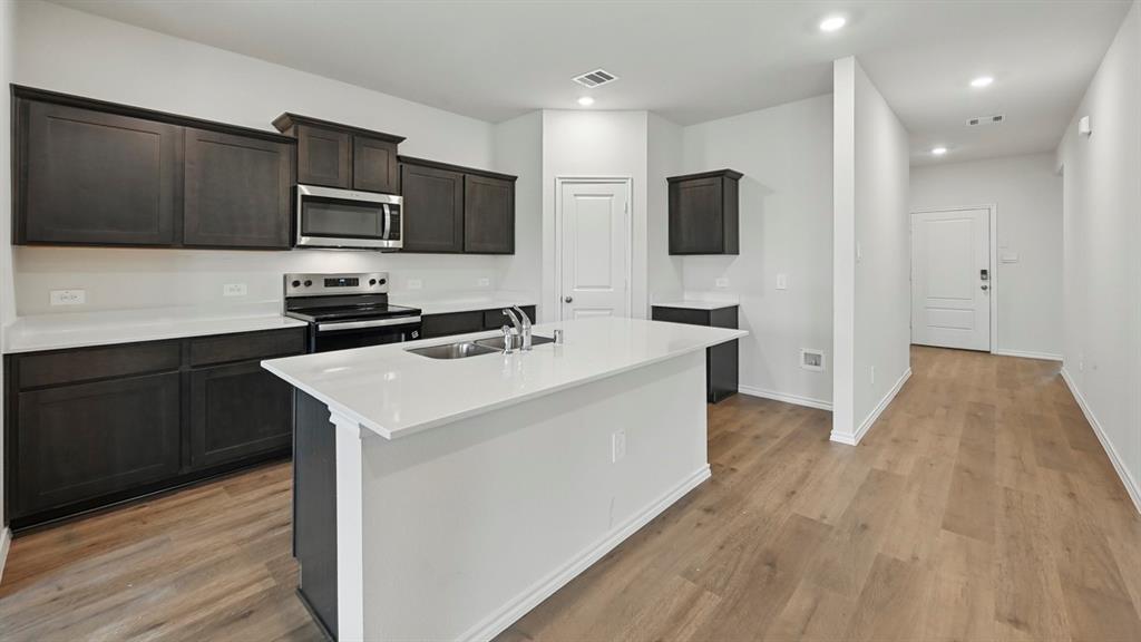 Kitchen featuring dark wood cabinetry, stainless steel appliances, white countertops, and a central island with an integrated sink