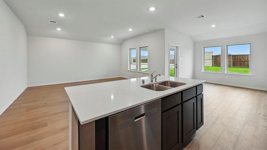 Kitchen island featuring a double basin stainless steel sink, stainless steel dishwasher, and dark cabinetry