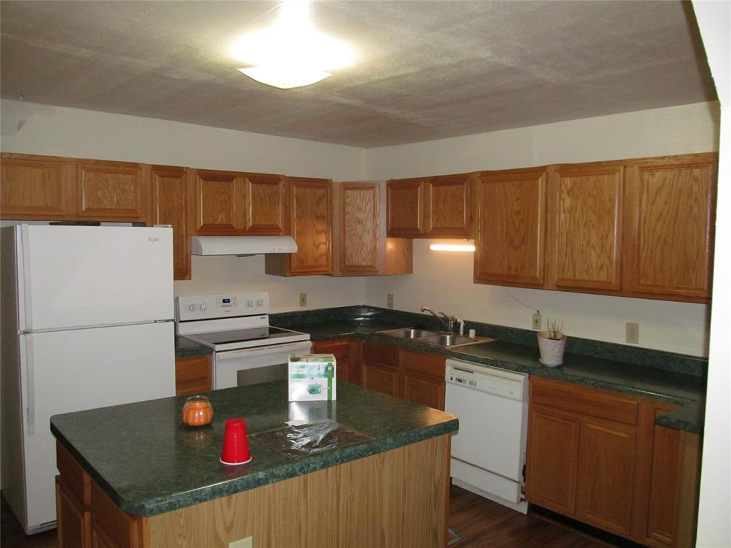 Kitchen featuring wood-finish cabinetry, green speckled countertops, white appliances, and a central island