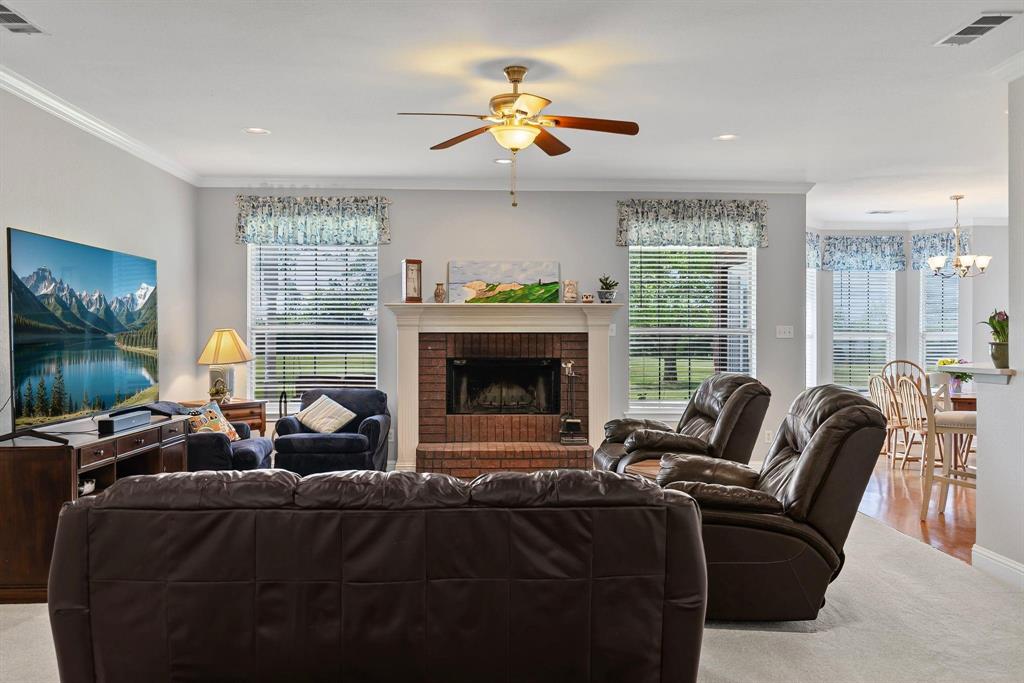 Living area featuring a brick fireplace with a white mantel, ceiling fan with integrated lighting, recessed lighting, and crown molding