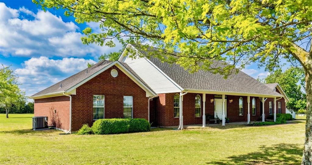 Brick exterior residence featuring a covered front porch with white columns, gabled rooflines, dark shingle roofing, and an expansive lawn