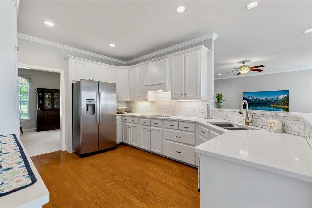 Modern kitchen featuring white cabinetry, stainless steel appliances, wood-finish flooring, recessed lighting, and a white tile backsplash