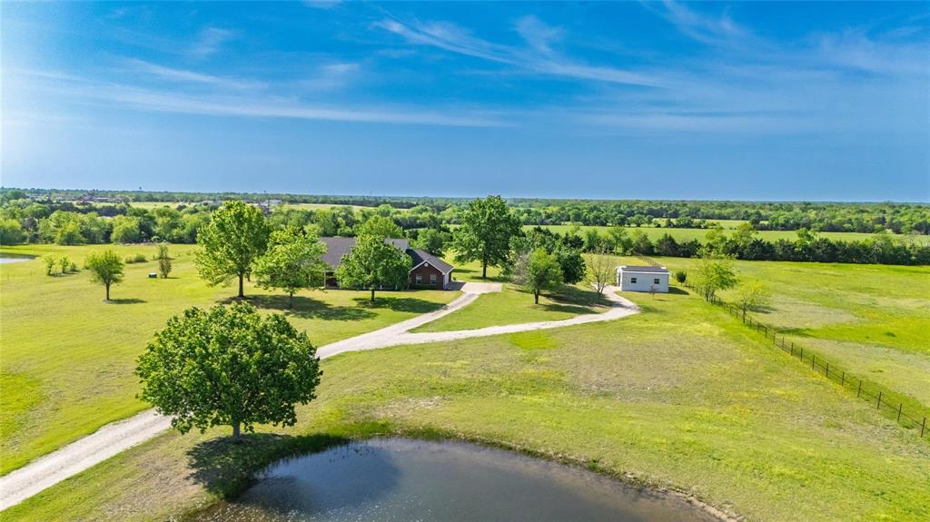 Expansive rural property featuring a main residence, a separate auxiliary building, a private pond, mature trees, and a perimeter fence