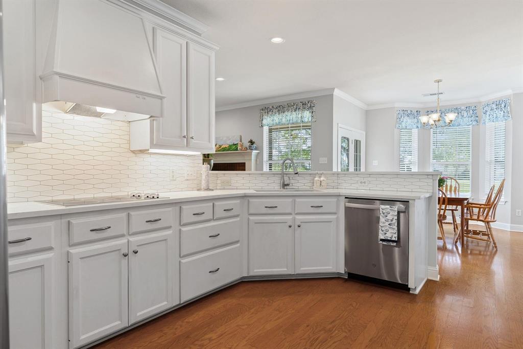 Kitchen featuring white cabinetry, light-toned countertops, a white hexagonal tile backsplash, stainless steel appliances, and wood-finish flooring