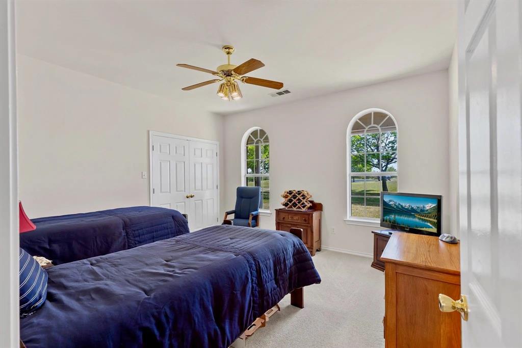 Spacious room featuring two arched windows with intricate upper grille work, a ceiling fan with integrated lighting, and carpeted flooring