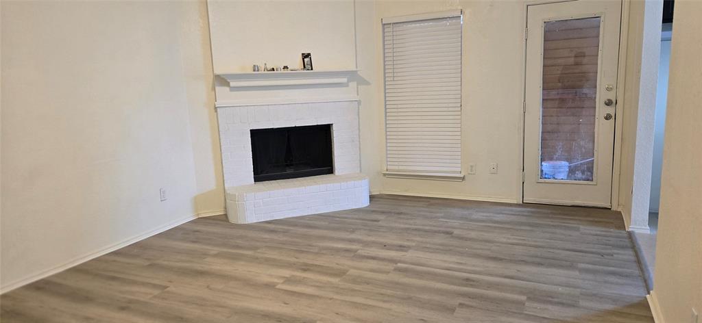 Living area featuring wood-finish flooring, a white brick fireplace with mantel, and a glass-paneled door