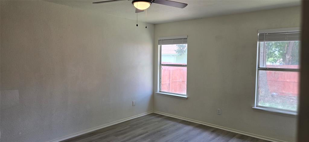 Room featuring two windows with blinds, a ceiling fan with integrated lighting, and wood-finish flooring