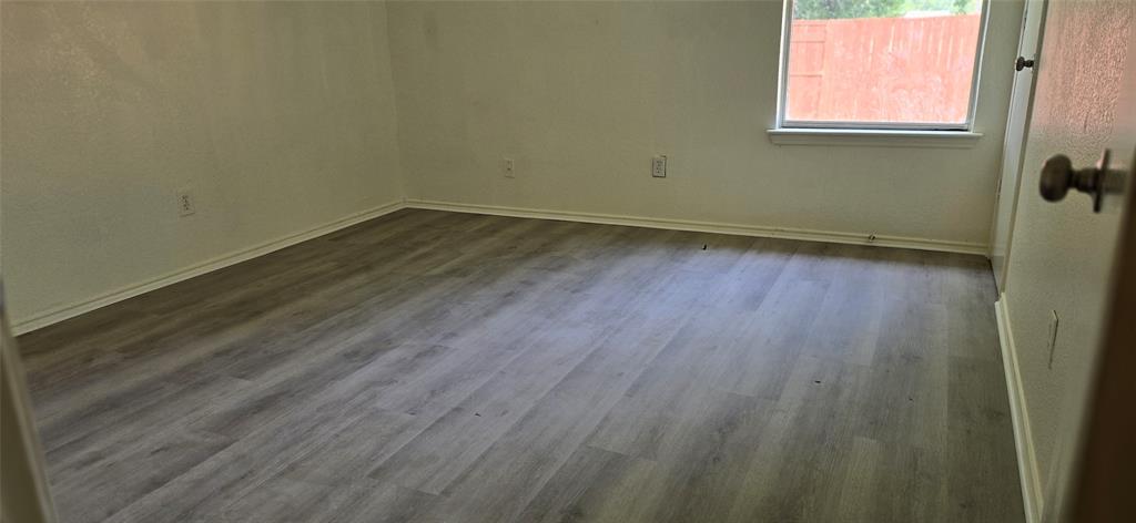 Interior room featuring wood-finish flooring, light-toned walls, a window with a white frame, and white baseboards