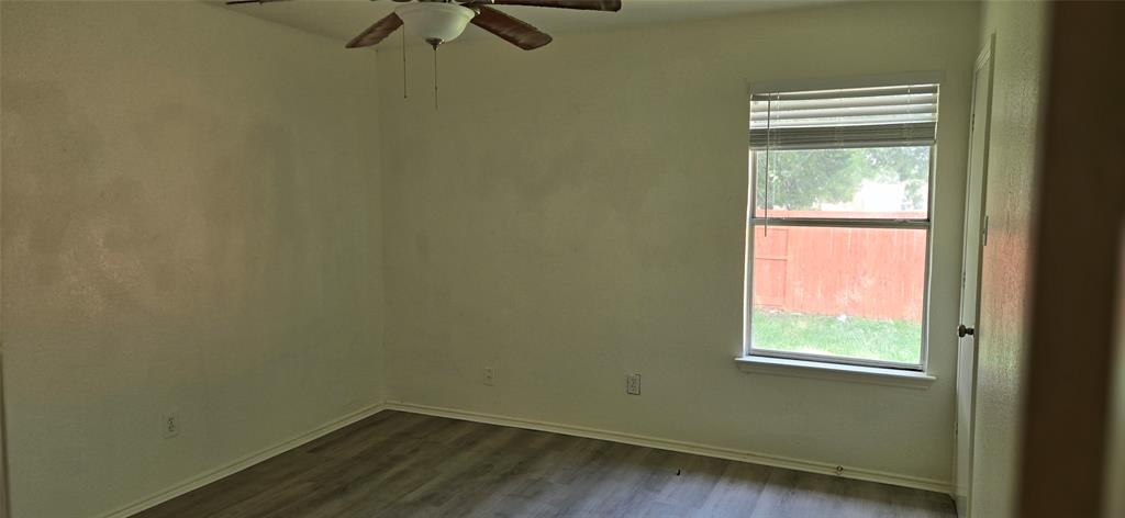 Interior space featuring wood-finish flooring, a ceiling fan with light fixture, and a window with blinds
