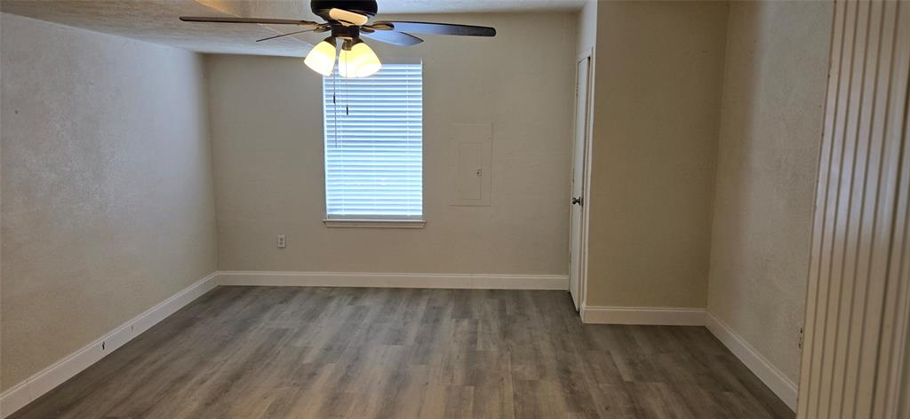 Room featuring wood-finish flooring, a window with blinds, a ceiling fan with integrated lighting, and a white trim package