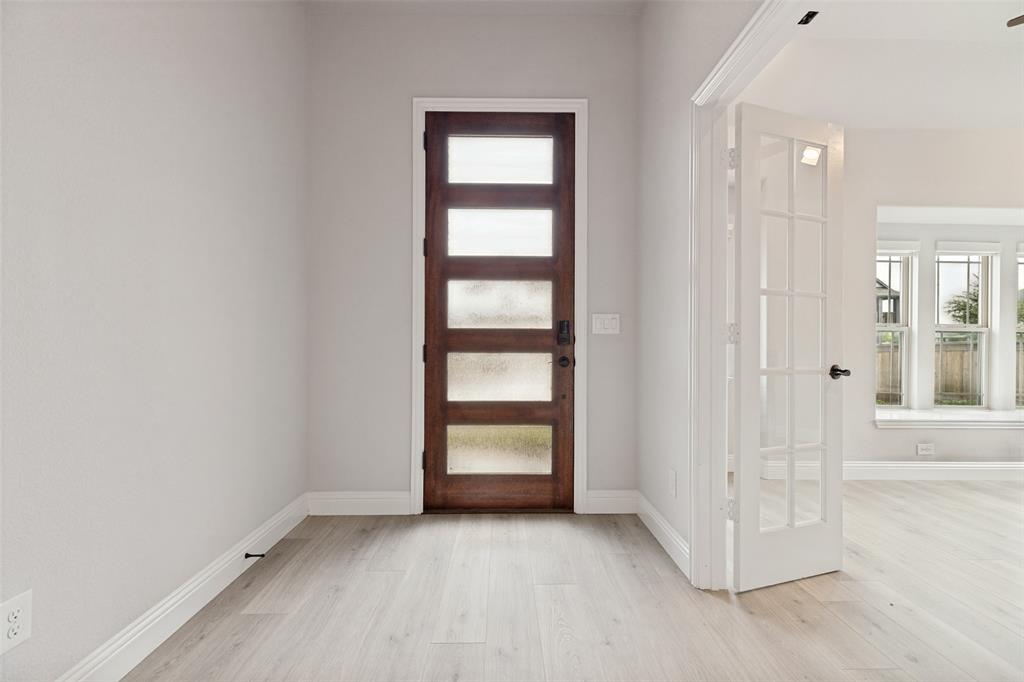 Entryway featuring a rich wood-finish front door with privacy glass panels, light wood-finish flooring, and crisp white baseboards