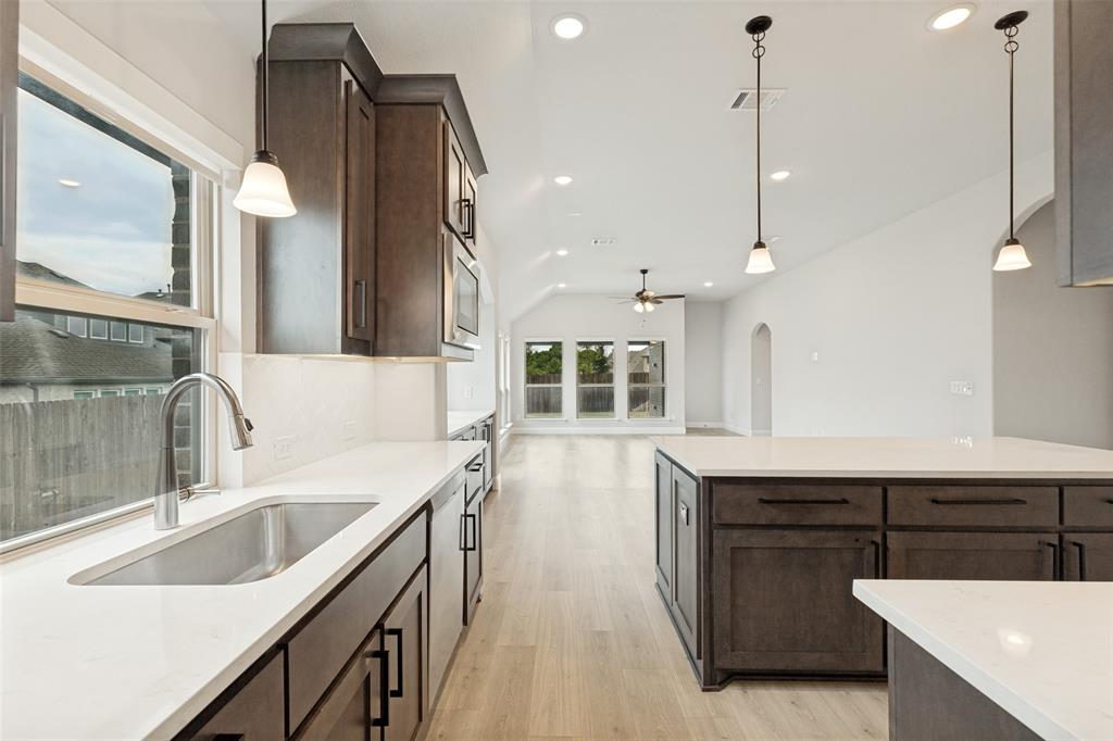 Kitchen featuring dark wood-finish cabinetry, white countertops, and a stainless steel sink with a gooseneck faucet