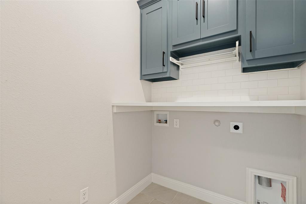 Utility space featuring blue shaker-style cabinetry with matte black hardware, a white subway tile backsplash, and a built-in drying rack