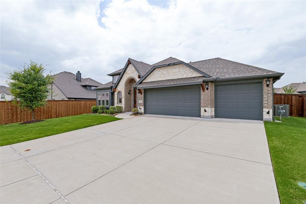 Stone and brick facade with an arched entryway, featuring a wide concrete driveway leading to a two-car garage