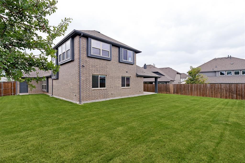 Expansive backyard featuring a manicured lawn, full privacy fencing, and a brick-clad residence with dark trim details