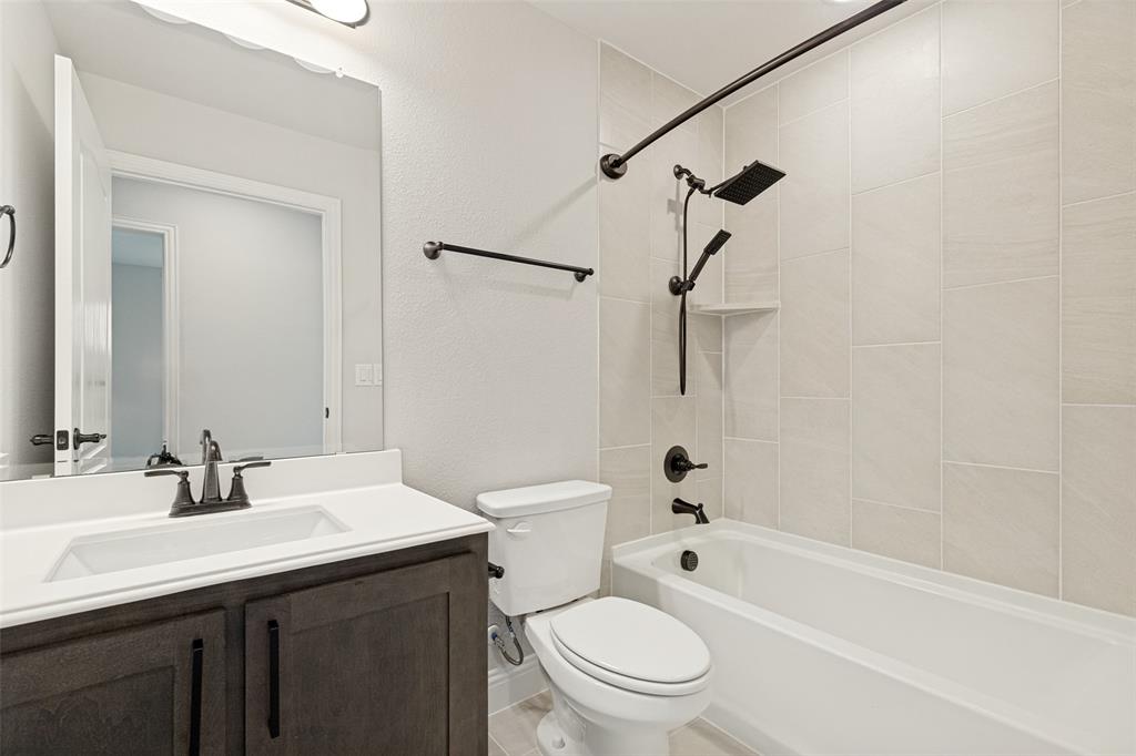 Bathroom featuring a dark wood-finish vanity with a white countertop and integrated sink, matte black fixtures, a white toilet, and a bathtub with light-toned tiled walls