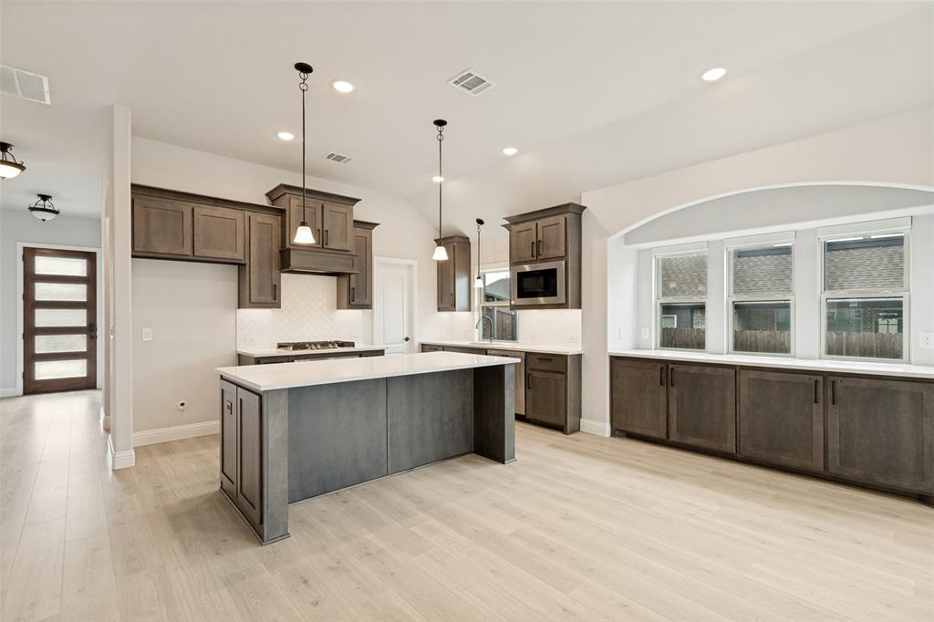 Expansive kitchen featuring a large central island with white countertop, recessed lighting, wood-finish flooring, and dark wood cabinetry