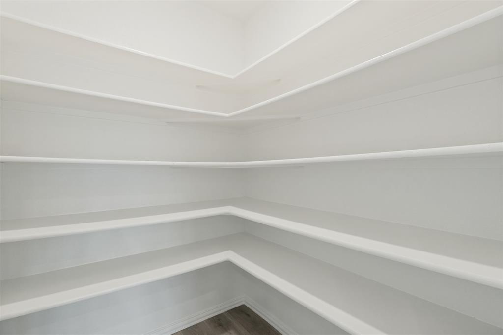 Walk-in pantry featuring extensive white shelving and wood-finish flooring