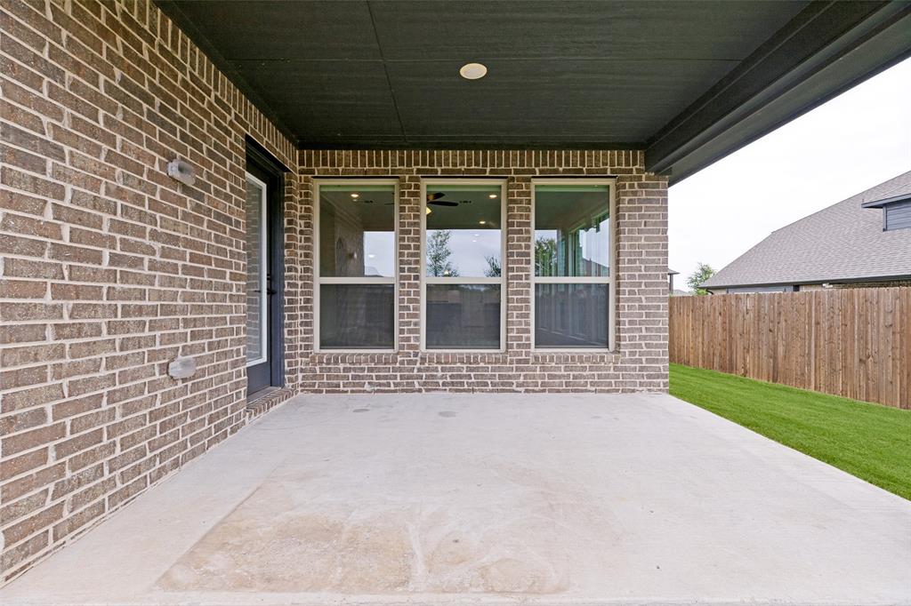 Covered concrete patio featuring a brick exterior, multiple windows, and a black exterior door