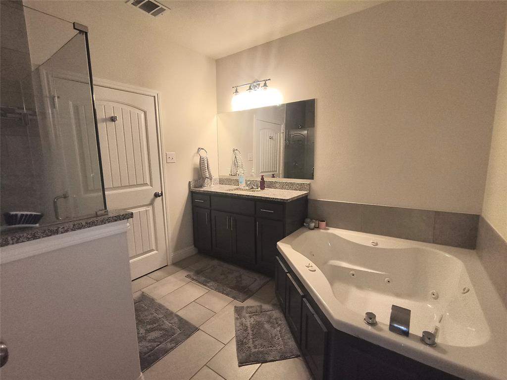 Bathroom featuring a corner jetted soaking tub, a dark wood-finish vanity with a light-toned countertop, a frameless mirror, and a glass-enclosed shower