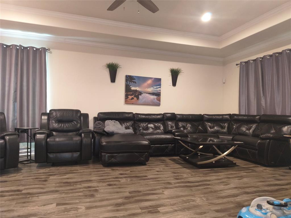 Spacious living area featuring wood-finish flooring, a tray ceiling, and crown molding